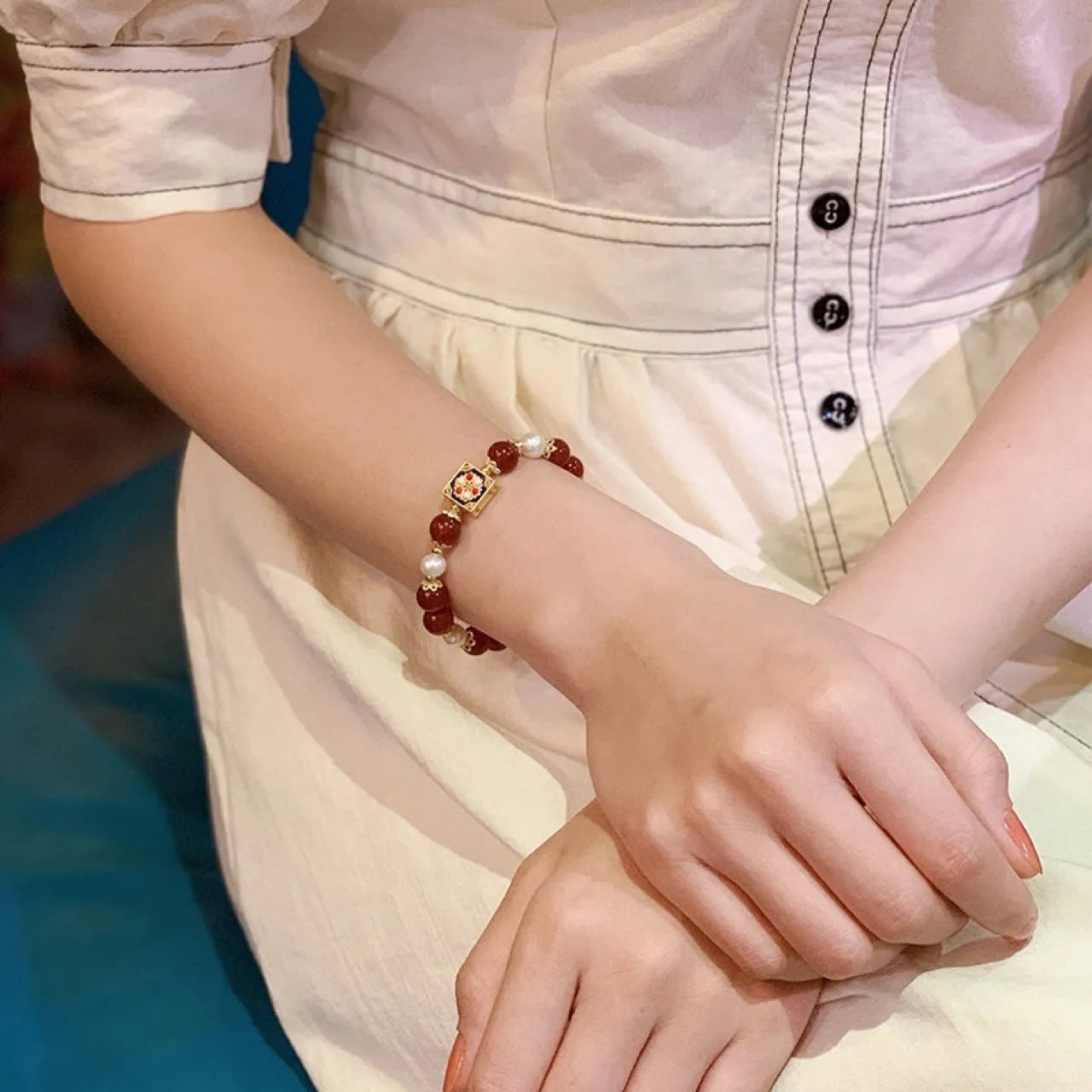 Red agate and pearl women's bracelet with constellation design on a wrist.