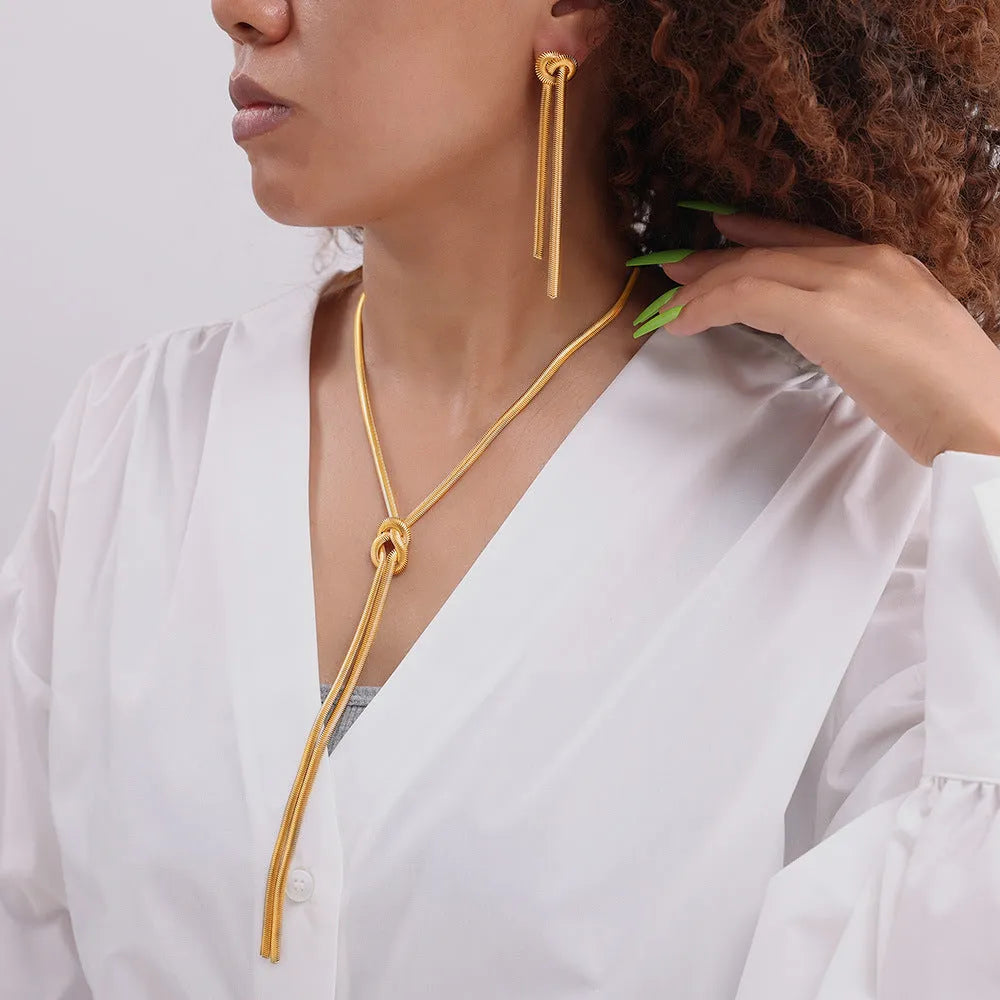 Gold long necklace with knotted tassel pendant and snake chain, shown with matching earrings.