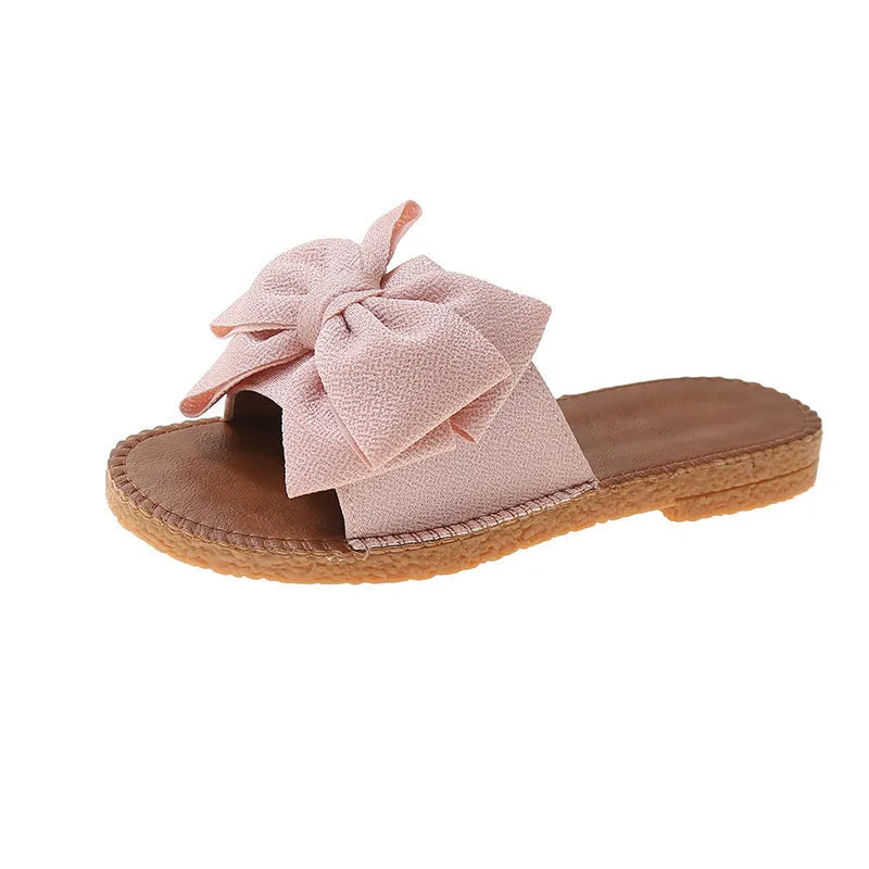 Women's beige slip-on suede sandals with a flat rubber sole and a small bow detail on the upper.