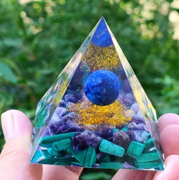 Clear epoxy resin pyramid ornament with natural crystal gravel inside on a wooden surface.