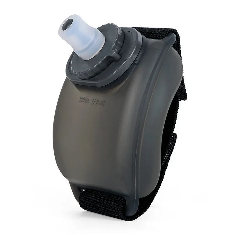Black silicone wrist water bottle with orange Velcro strap secured around a wrist, showing bite valve.