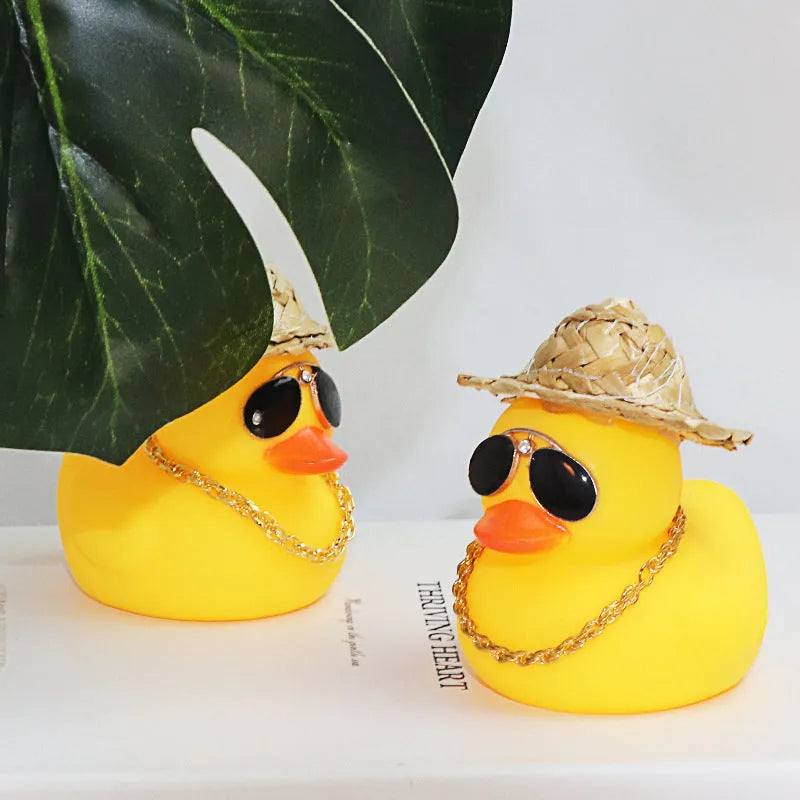 Yellow duck cartoon character wearing a straw hat, a car dashboard ornament with miniature sunglasses accessory.