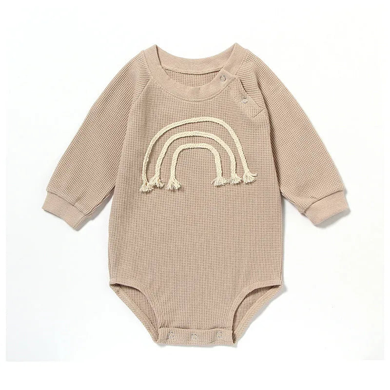 Long-sleeved waffle cotton baby romper in a neutral colour on a hanger, showing the triangular climbing front closure.