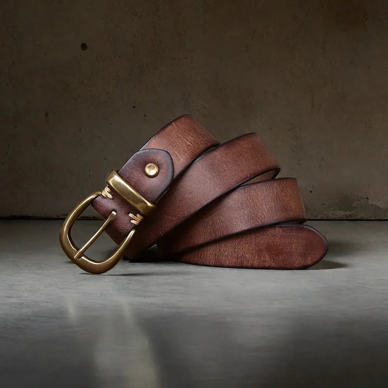 Men's black cattlehide leather jeans belt with a copper pin buckle on a wooden background.