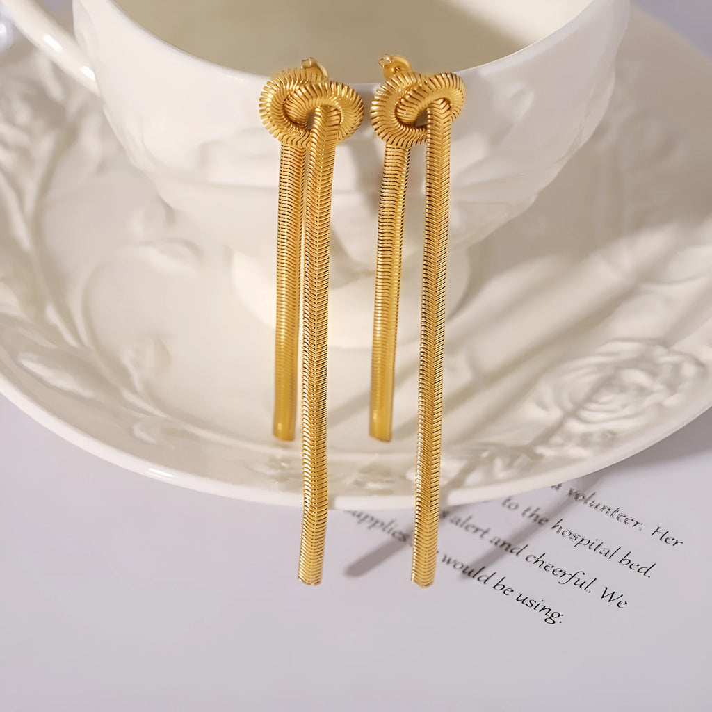 Gold long necklace with knotted tassel pendant and snake chain, shown with matching earrings.