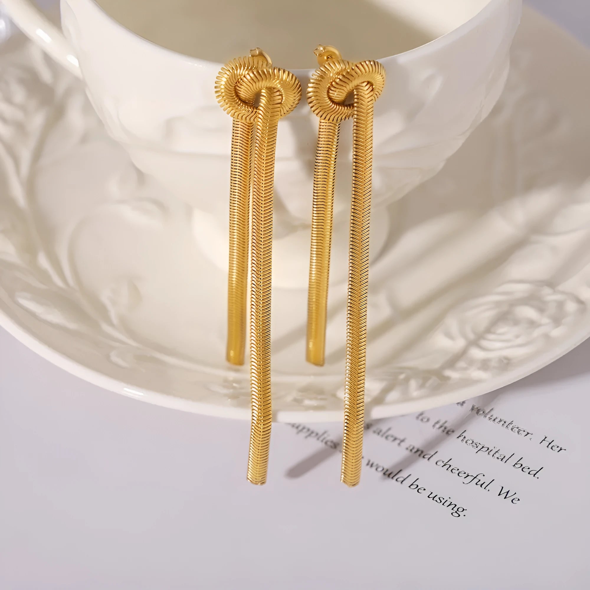 Gold long necklace with knotted tassel pendant and snake chain, shown with matching earrings.
