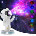 White Exit Astronaut Starlight Projection Lamp with USB cable and remote control on a table, projecting a blue starry light effect