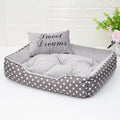 Polka dot square dog bed with matching embroidered pillow in grey, shown in a home setting.