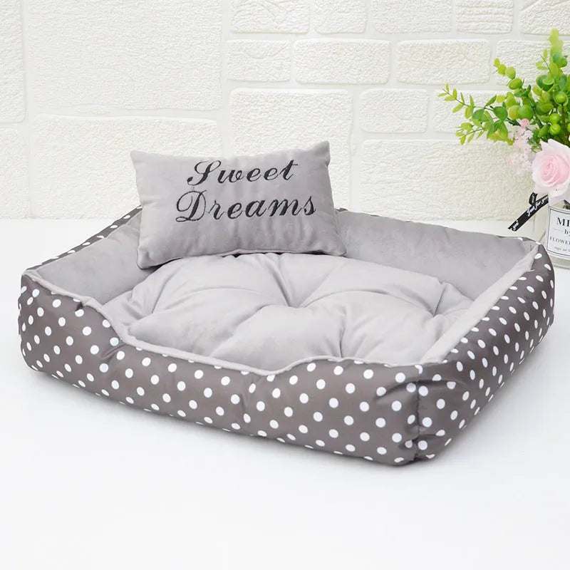 Polka dot square dog bed with matching embroidered pillow in grey, shown in a home setting.