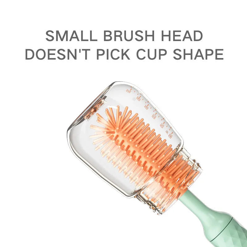 Pink and green electric baby bottle cleaning brush with rotating silicone head on a table