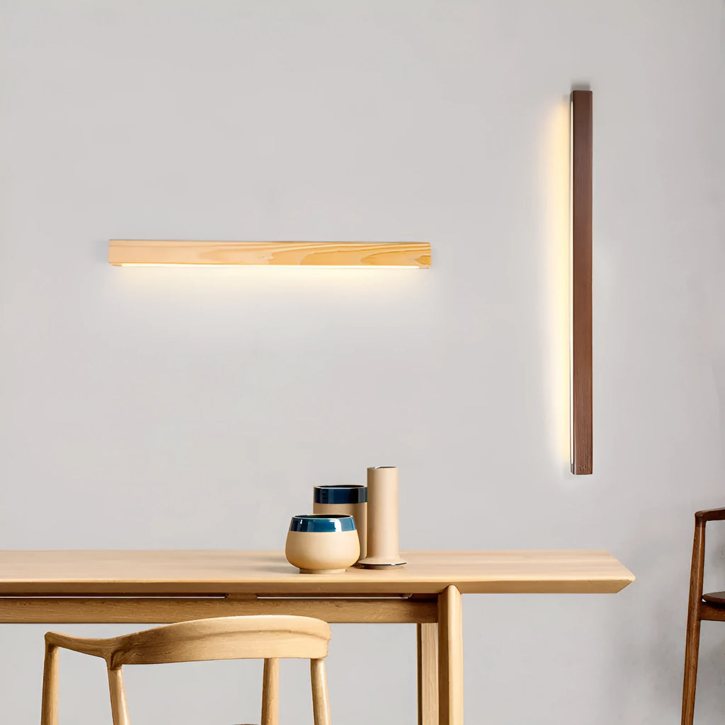 Long, slim walnut-coloured wooden wall lamp with integrated LED light, shown in a minimalist room setting.