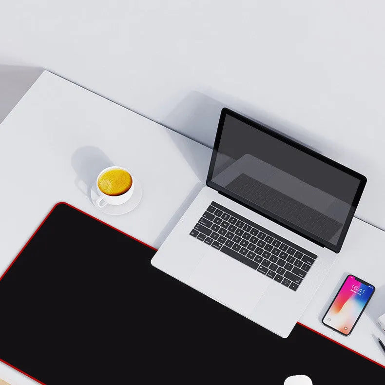 Long black desk pad with stitched edges on a wooden desk, with keyboard and mouse placed on top.