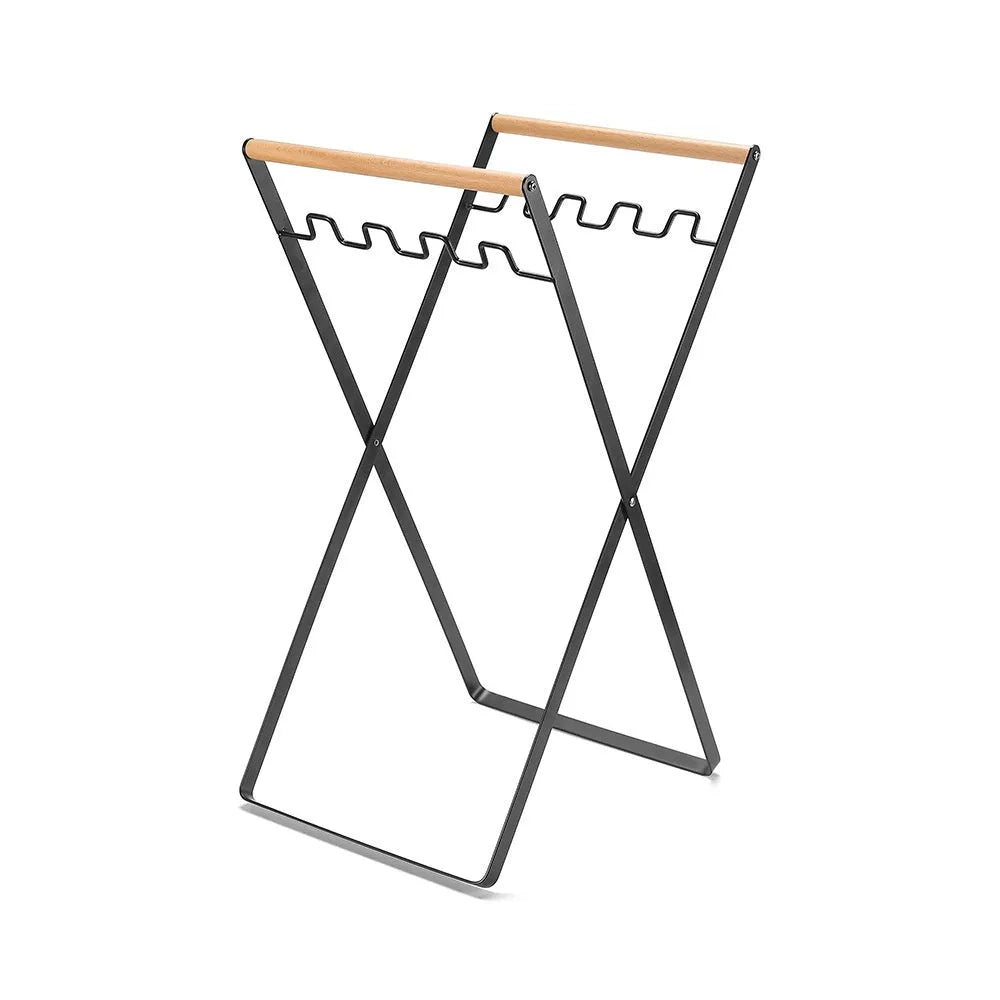 Black iron folding trash storage rack with a wooden handle for hanging bin bags.
