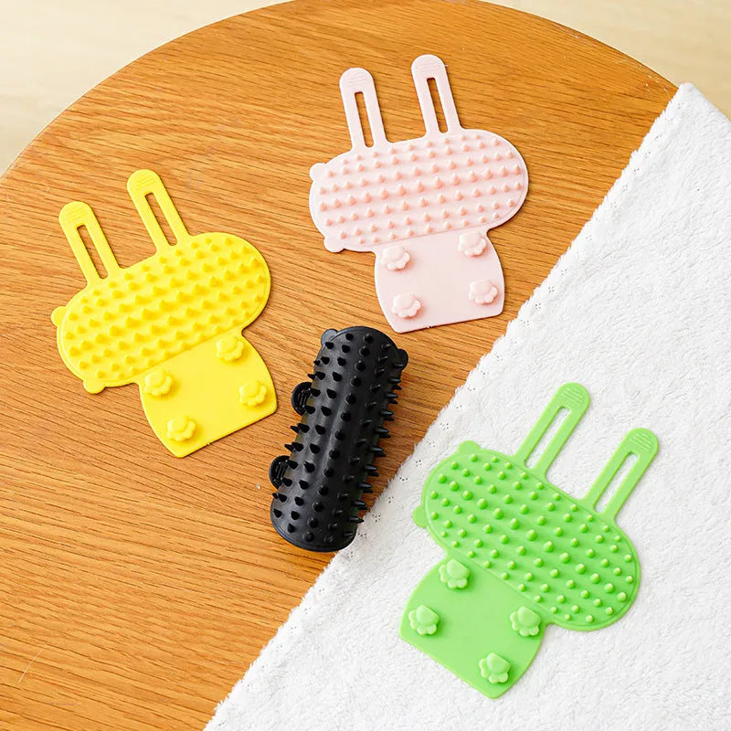 Black silicone cat grooming brush with comb teeth and an adjustable mounting strap.