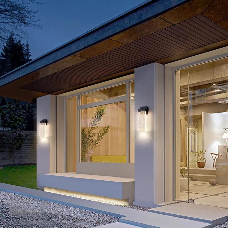 Black stainless steel outdoor LED wall lamp mounted on a wall, showing its rectangular shape and warm light emission.