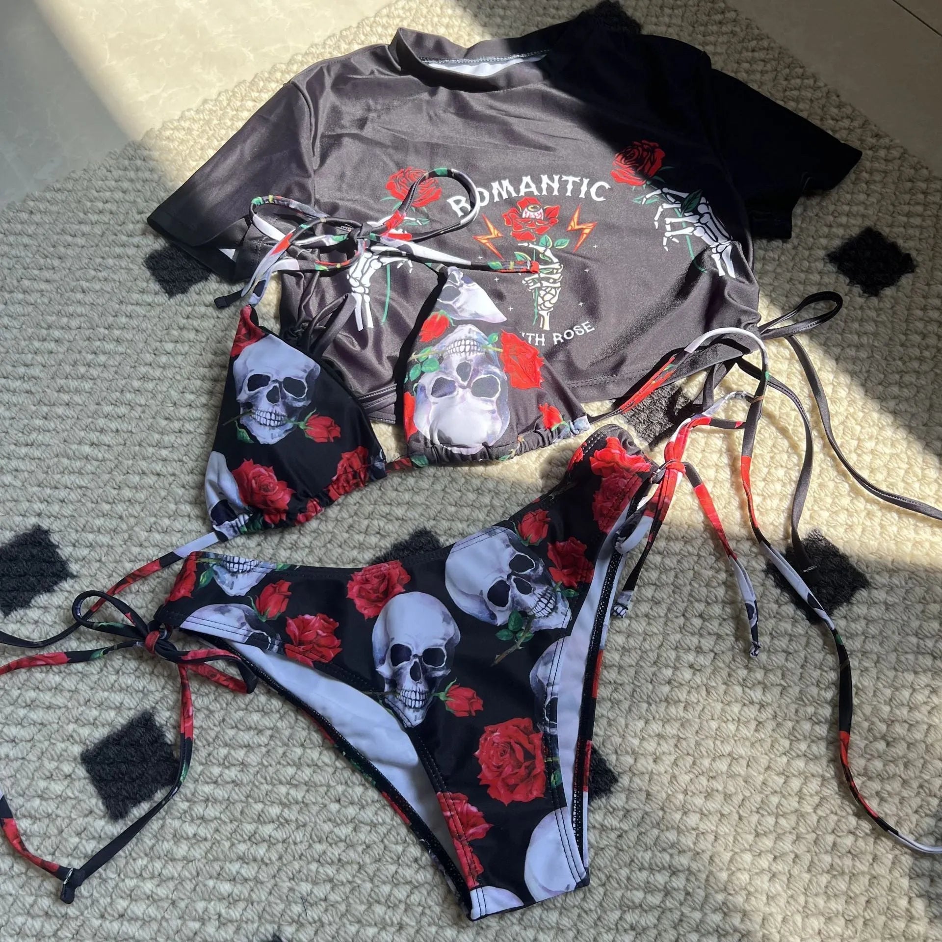 Women's red three-piece swimwear set with skull and rose print showing cropped top, bikini bottoms, and shorts