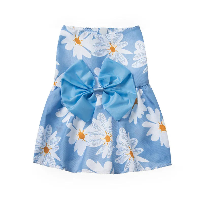 A dog or cat wearing a thin orange princess dress with a large floral butterfly knot bow.