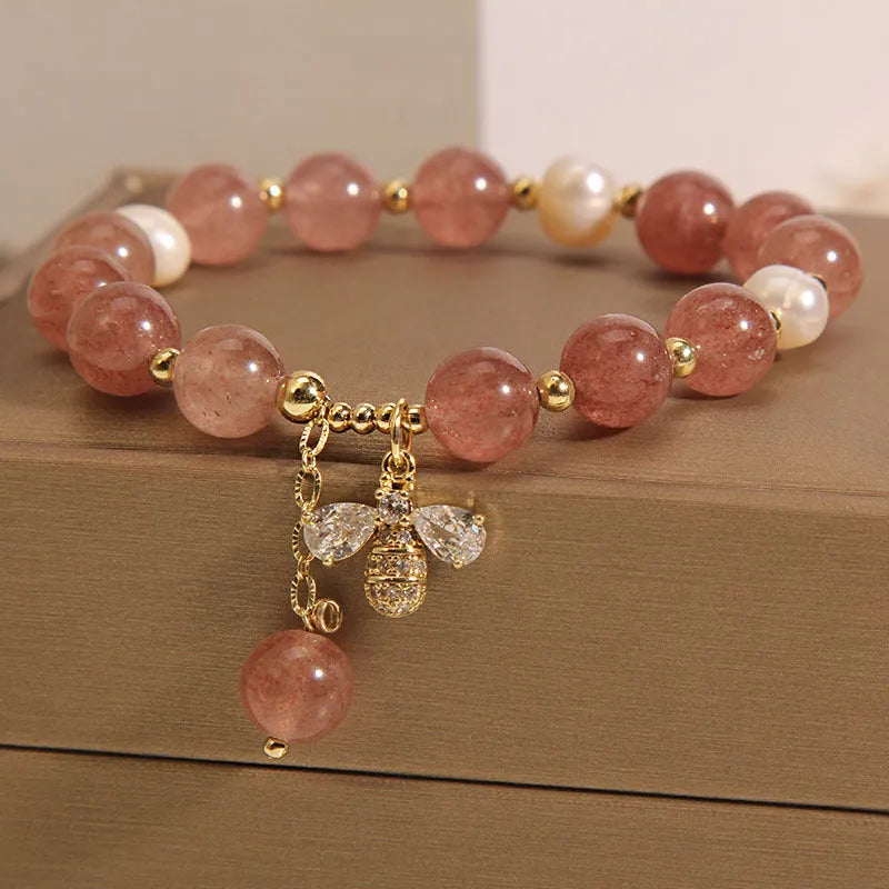 Adjustable pink strawberry quartz bracelet with three freshwater pearls and sparkling zircon charms on a wrist.
