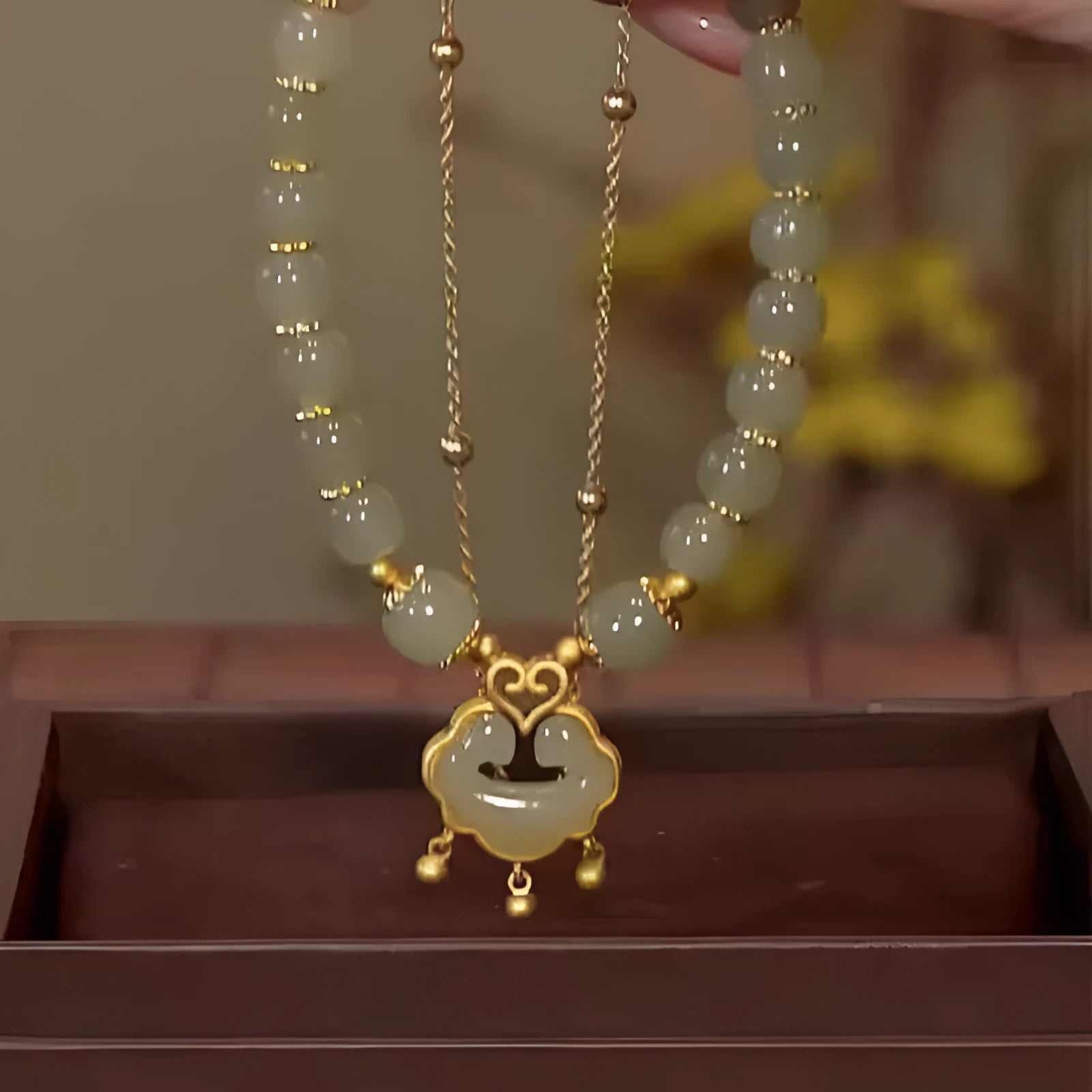 Close-up of a women's green double-layer bracelet with a drop-shaped Xiangyun safety lock pendant.