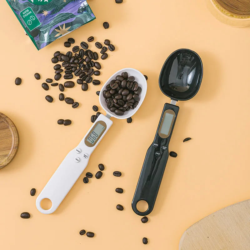White digital kitchen scale with LCD screen displaying weight, shown next to a measuring spoon.