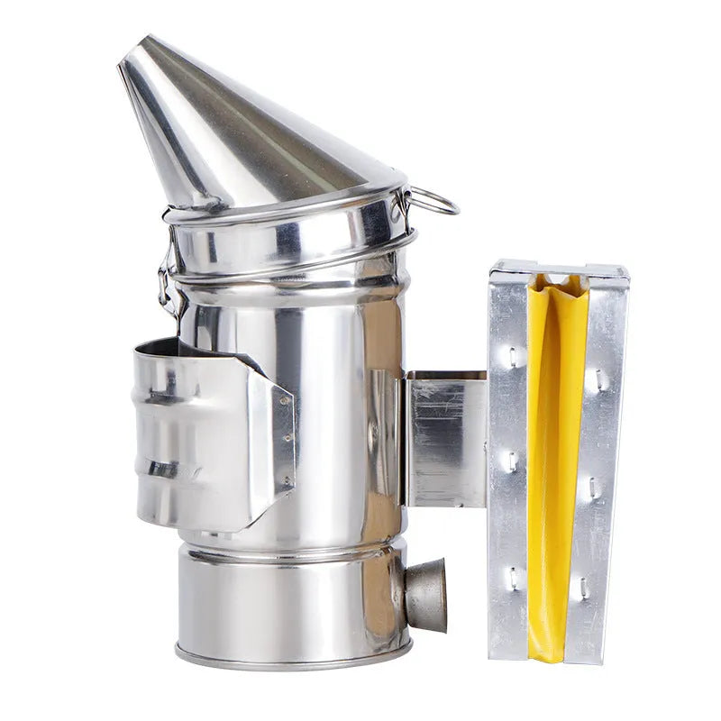 Stainless steel bee smoker with leather bellow on a wooden table against a blurred outdoor background