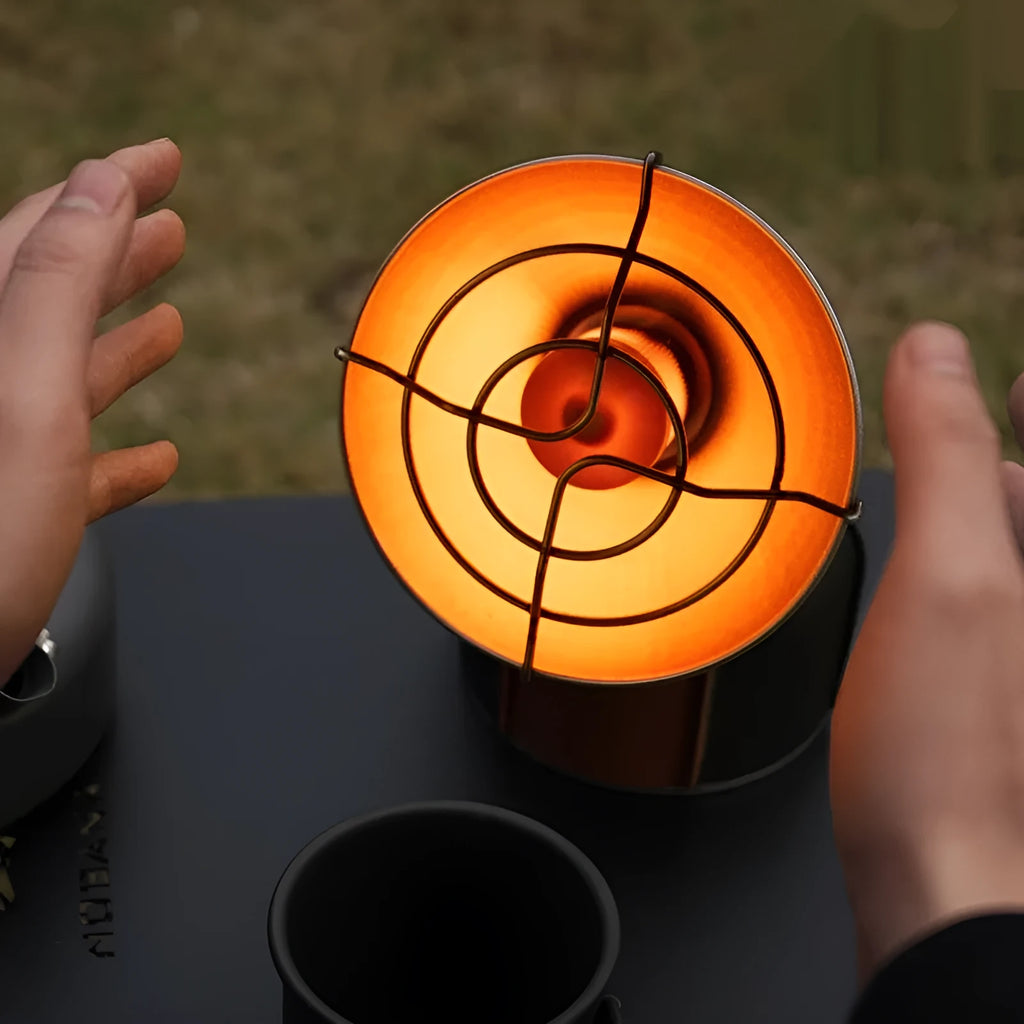 Black and orange portable outdoor heating stove with automatic ignition on a camping table.