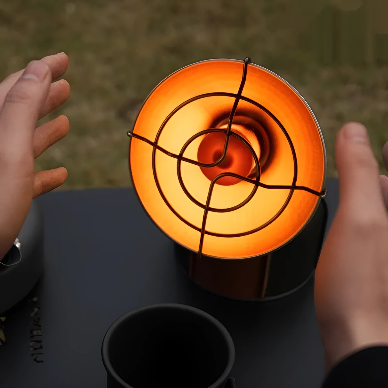 Black and orange portable outdoor heating stove with automatic ignition on a camping table.