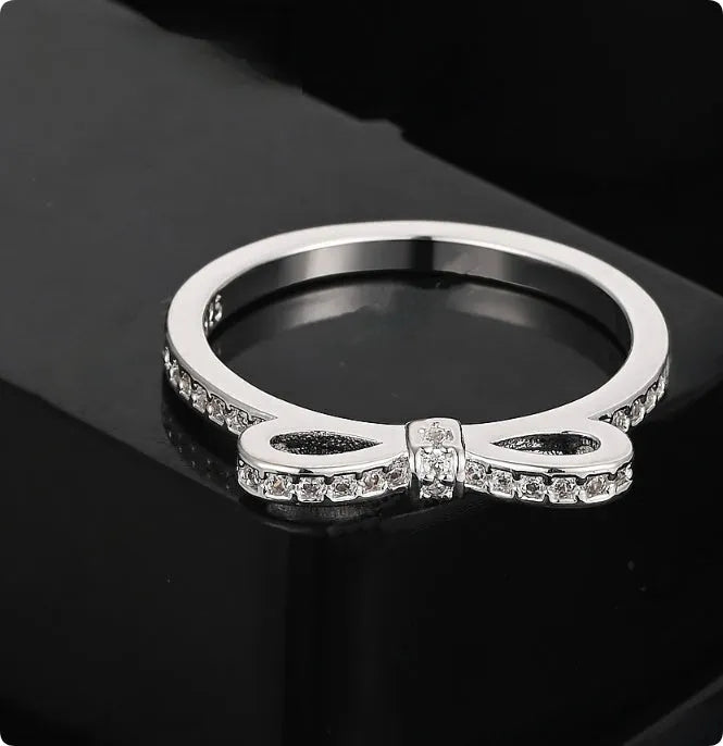 Silver electroplated bow ring with sparkling zircon crystals on a finger.