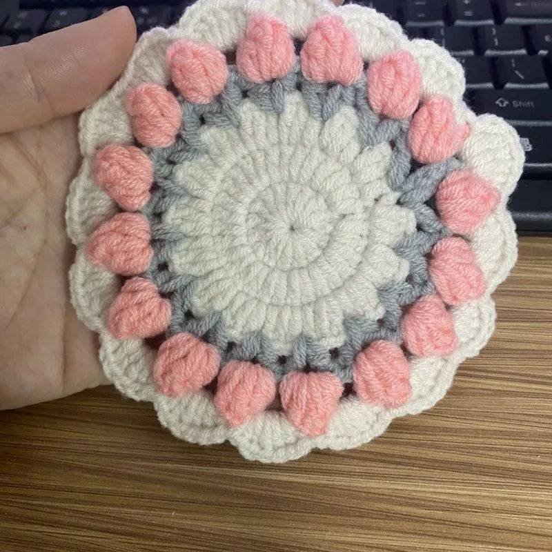 Set of four handmade woven floral coasters in pink, purple, red, and yellow on a wooden table.