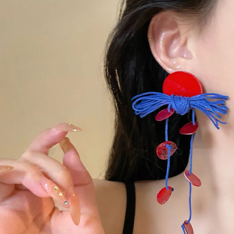 Handmade geometric cloth earrings with a blue resin flower and silver detail on a white background.