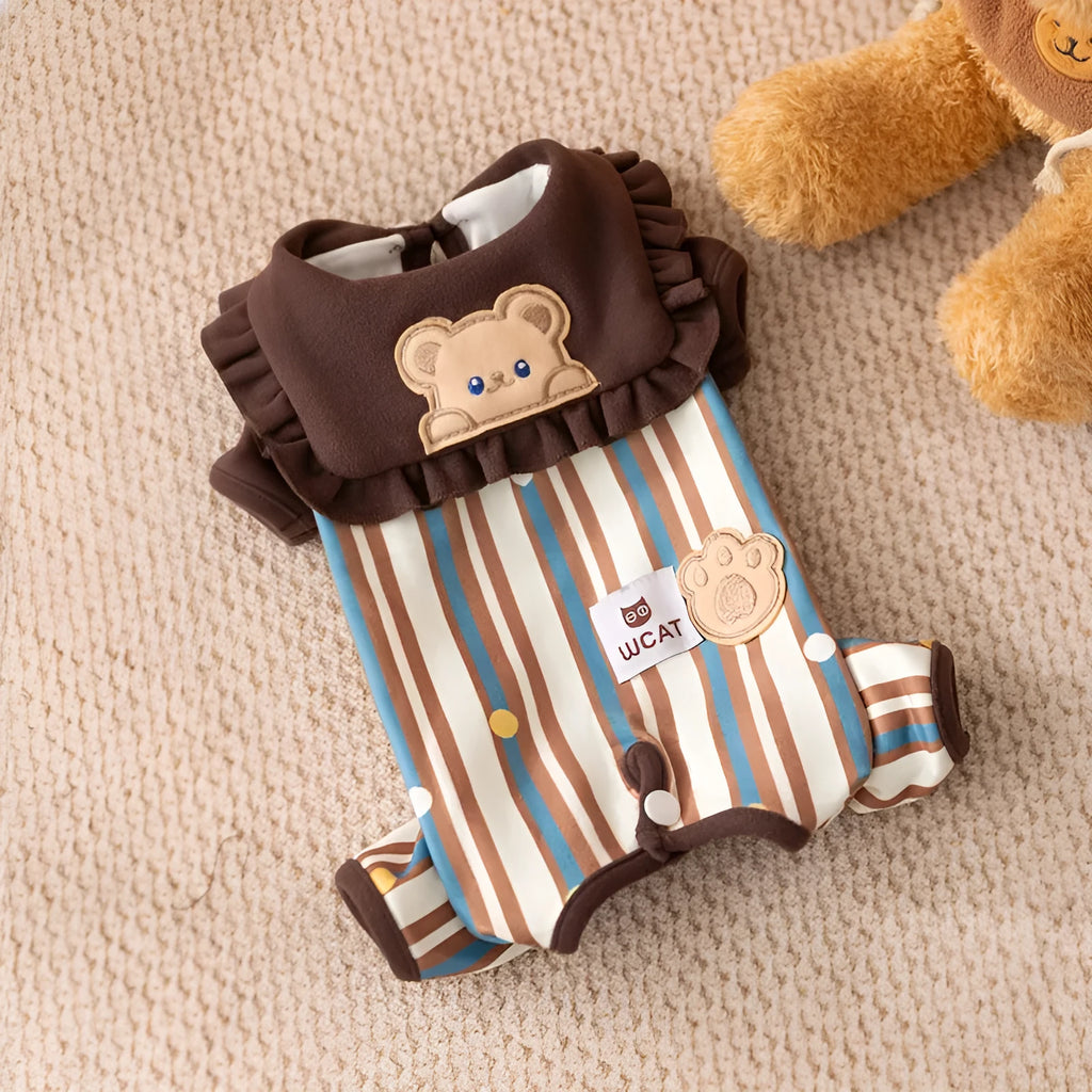 Small brown dog wearing a blue and brown striped onesie with ruffled collar and bear patch