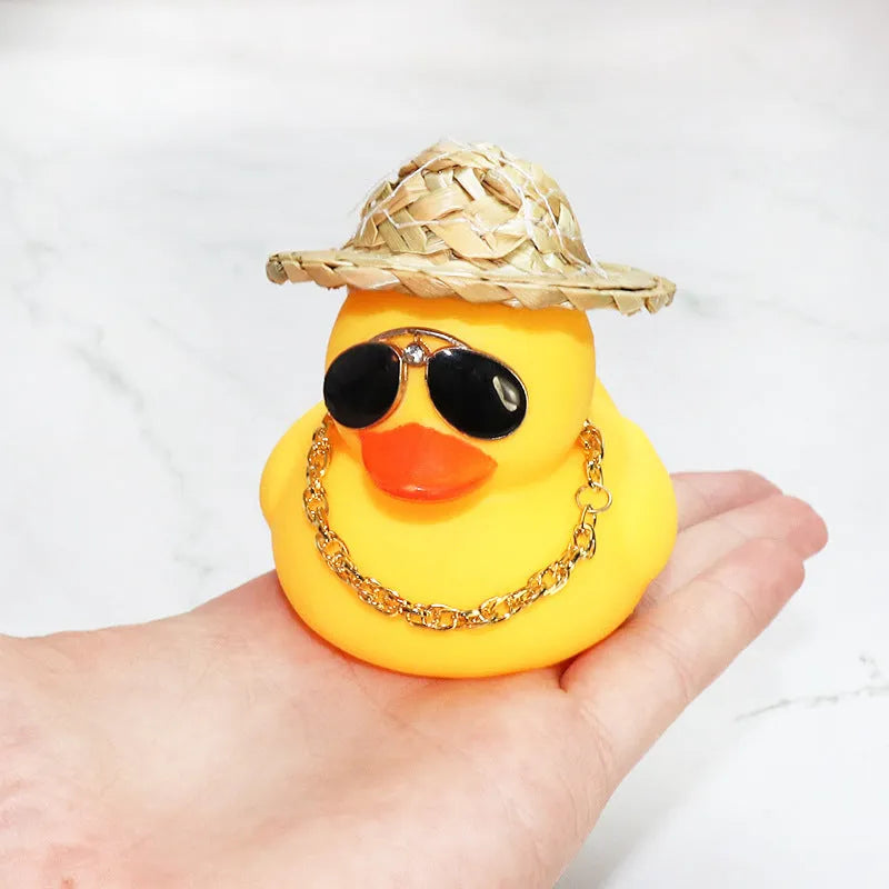 Yellow duck cartoon character wearing a straw hat, a car dashboard ornament with miniature sunglasses accessory.