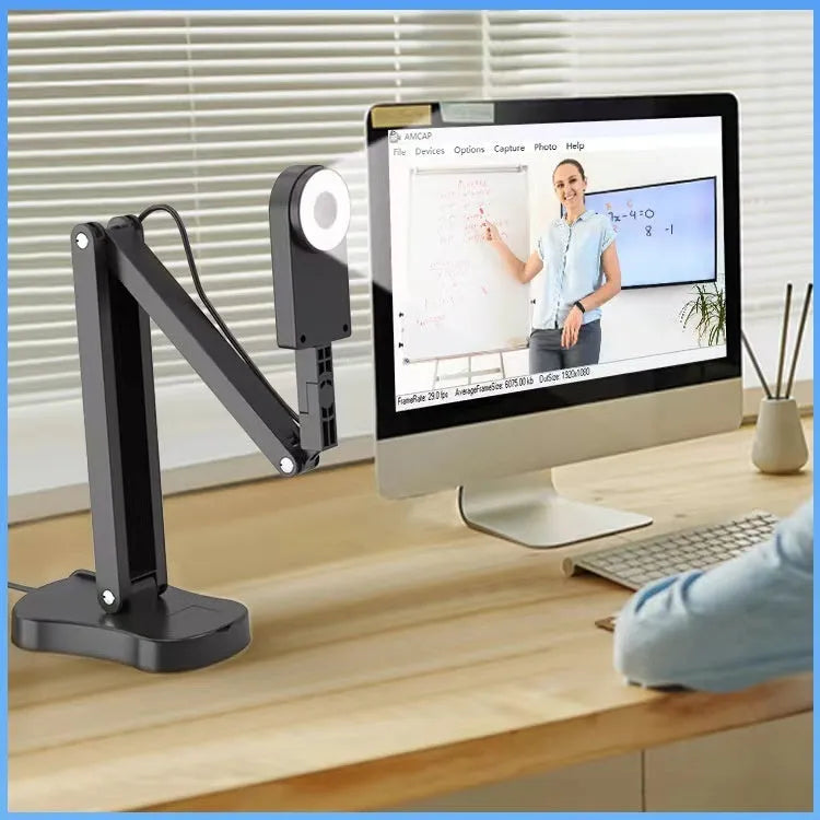Black USB computer webcam with microphone on a desk, showing its compact design and attached data cable.