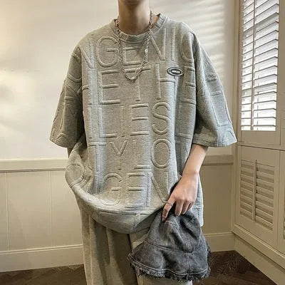 Men's grey loose-fit short sleeve t-shirt featuring a raised three-dimensional letter design on the front.