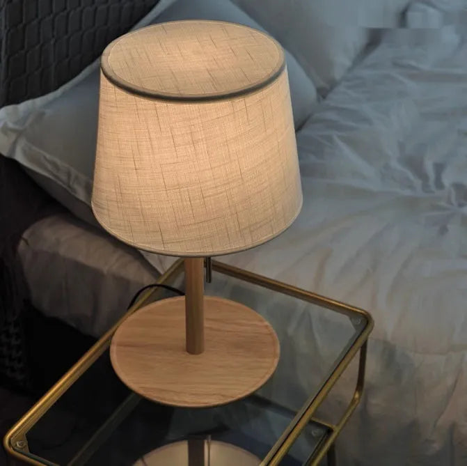 Walnut coloured solid wood bedside lamp with a white cloth shade and a cable switch.