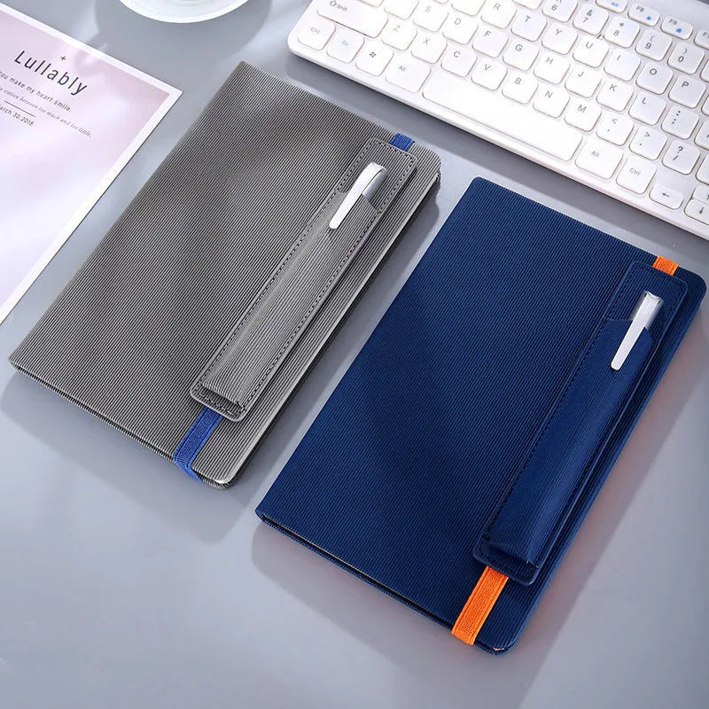 A5 faux leather notebook with pen insert and strap, open on a desk showing lined pages
