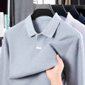 Men's grey loose fit cotton polo shirt with long sleeves and a lapel collar on a hanger.