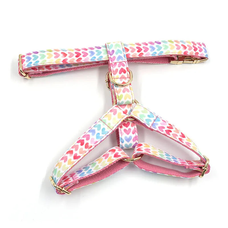 Pink dog harness with a gold buckle and colourful heart-shaped stone decoration on an adjustable polyester strap.