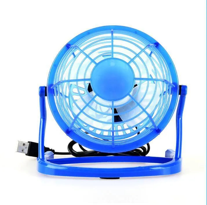 Small black USB desk fan with adjustable tilt on a wooden desk next to a laptop