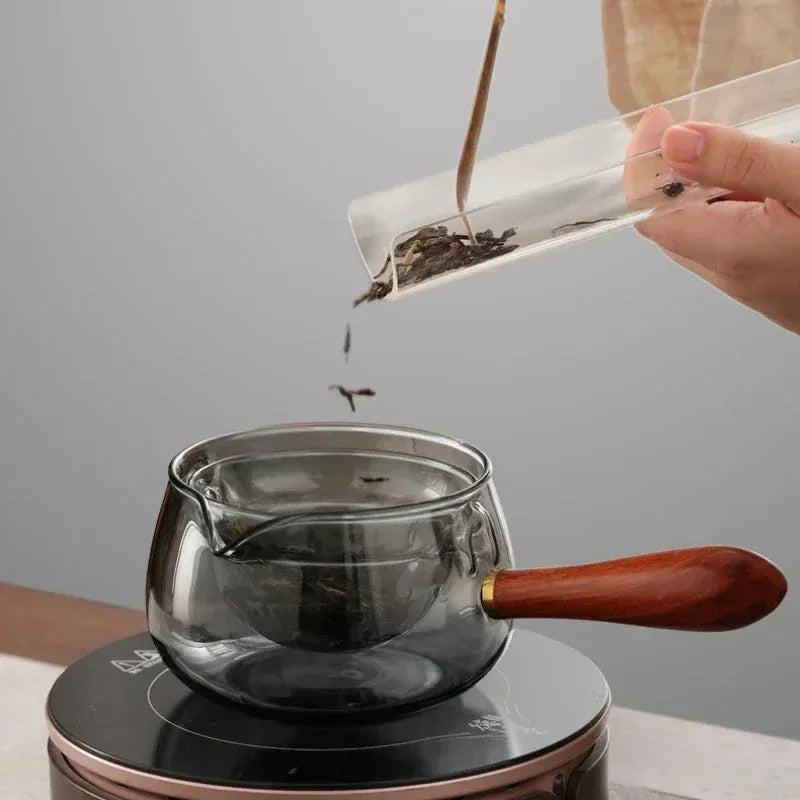 Transparent rotary glass teapot with wooden handle and built-in tea infuser on a table.