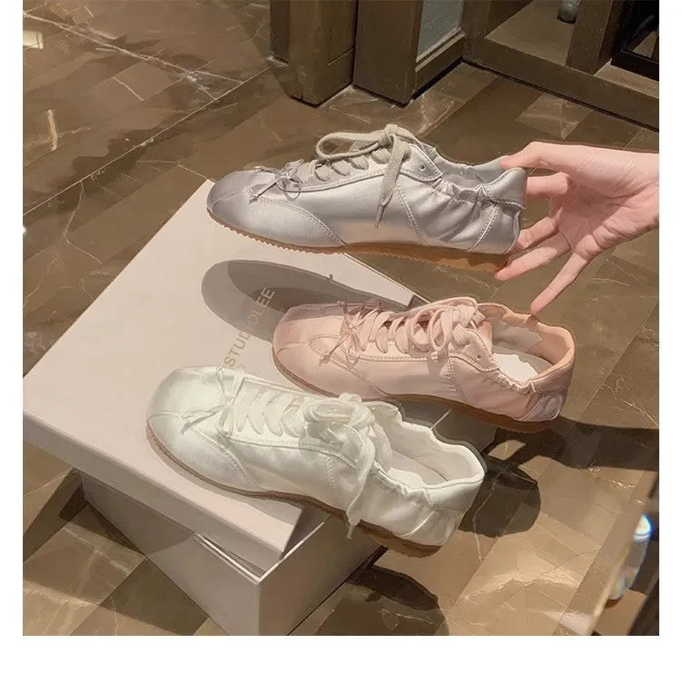 Women's champagne pink satin ballet flats with round toe and lace-up front, shown on a white background.