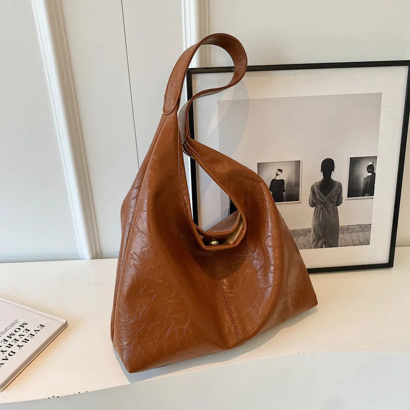Soft black PU leather shoulder bag with large compartment and adjustable strap on a plain background.