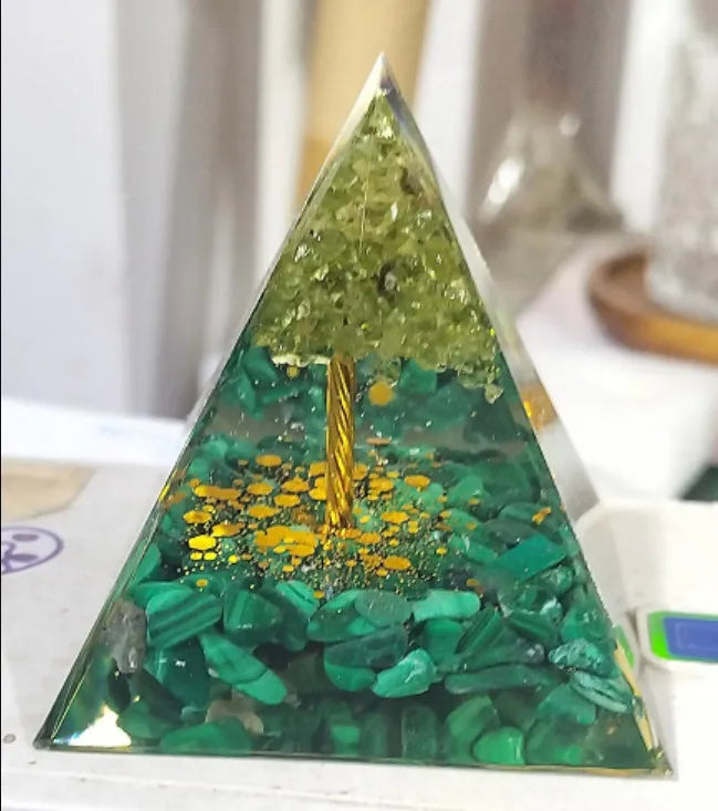 Clear epoxy resin pyramid ornament with natural crystal gravel inside on a wooden surface.