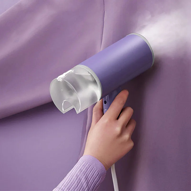 Foldable handheld clothes steamer in grey lotus root purple on a table.