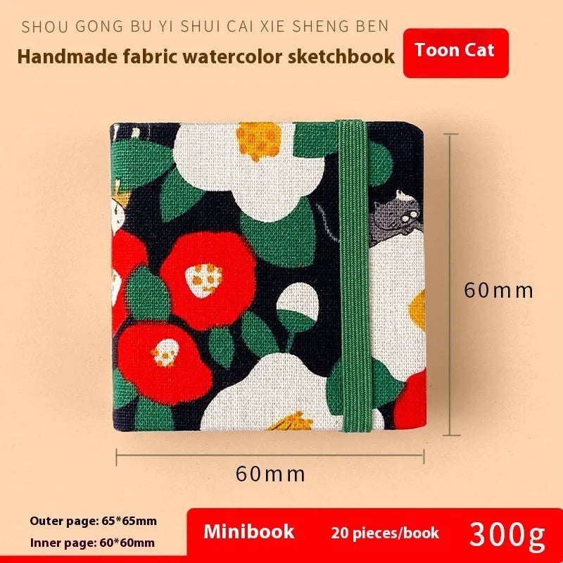Feiluniao handmade fabric watercolour notebook with illustrated cover, open to show blank paper pages.