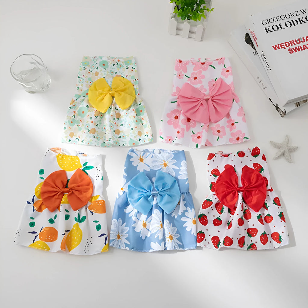 A dog or cat wearing a thin orange princess dress with a large floral butterfly knot bow.