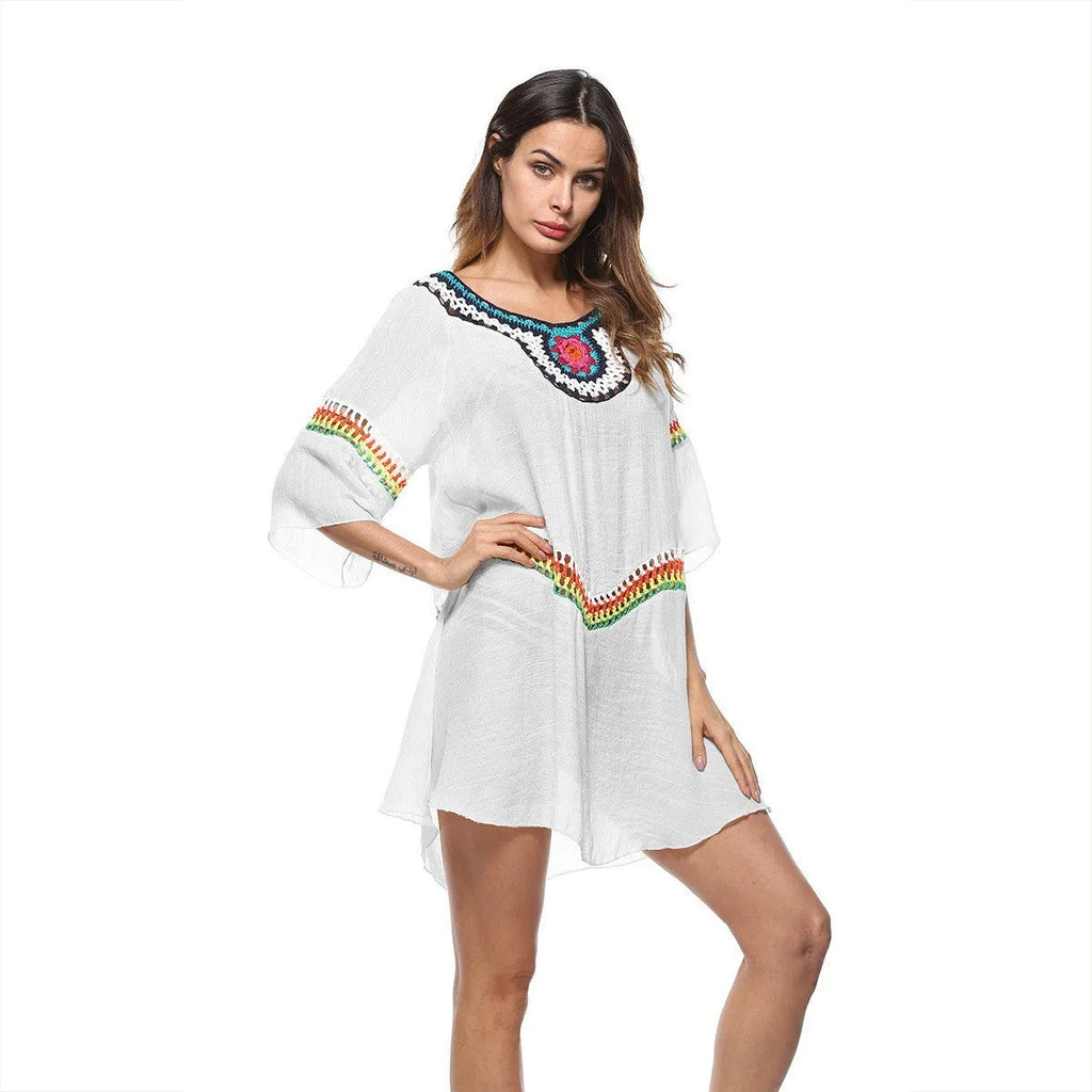 Woman wearing a crocheted white sun protection beach cover-up by the water.