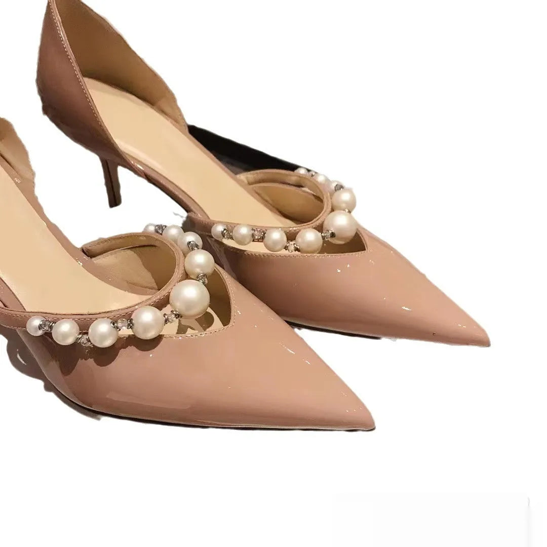 Women's black patent leather stiletto high heels with pointed toe and pearl decoration on display.