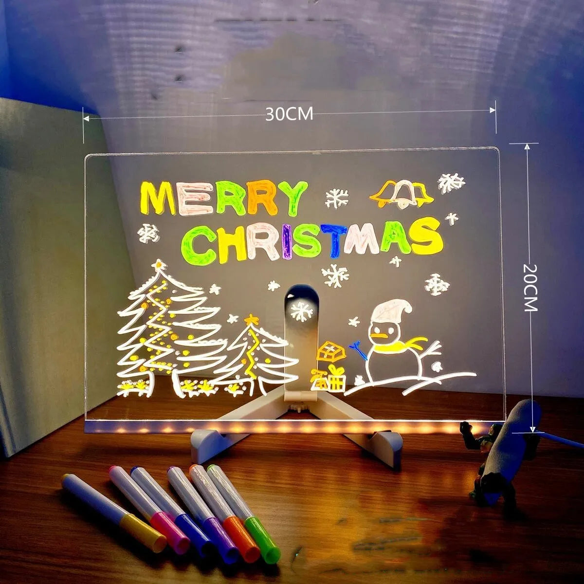 DIY acrylic LED message board lamp on a desk with colourful writing, showing USB cable and pens.