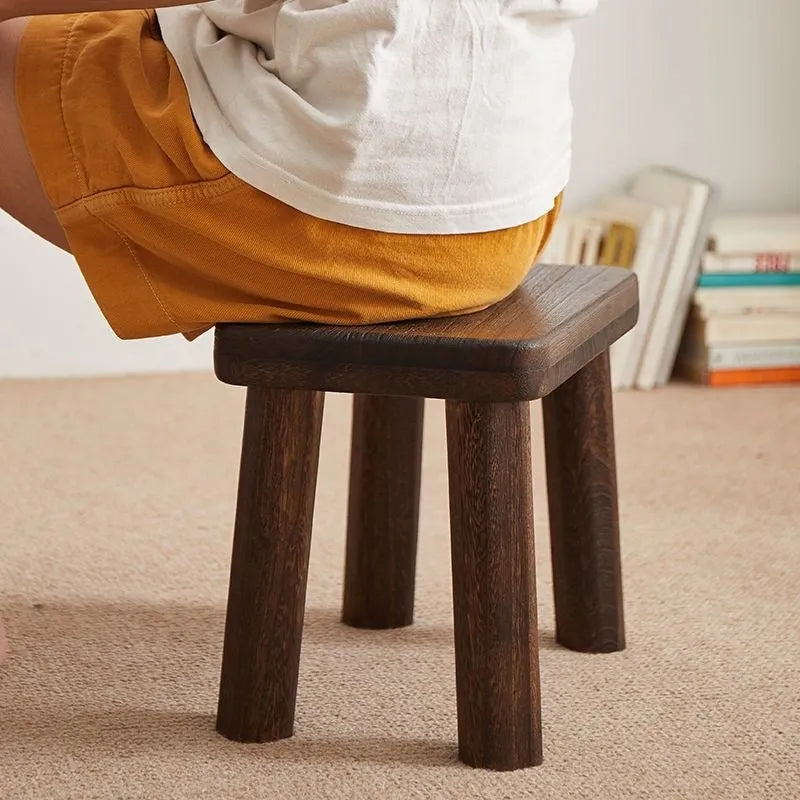 Solid wood distressed finish changing stool with bracket structure legs in a living room setting.